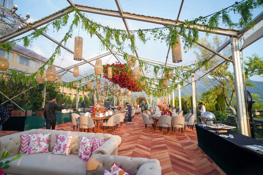 Glass marquee setup with hanging lanterns and greenery