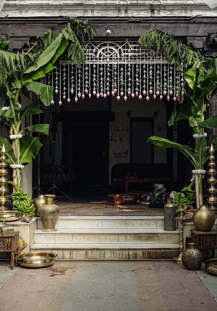 Entrance styled with banana plants, brass urns and floral torans for a heritage evening