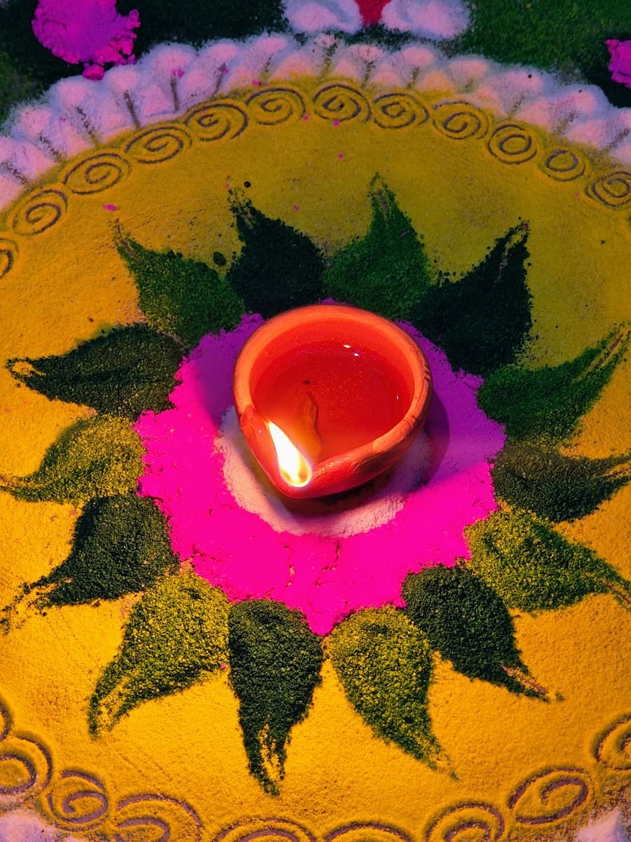 Hand-painted alpana floor art with a lit clay diya