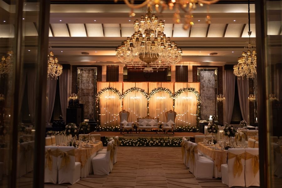 Banquet hall wedding setup with lit stage and gold table styling