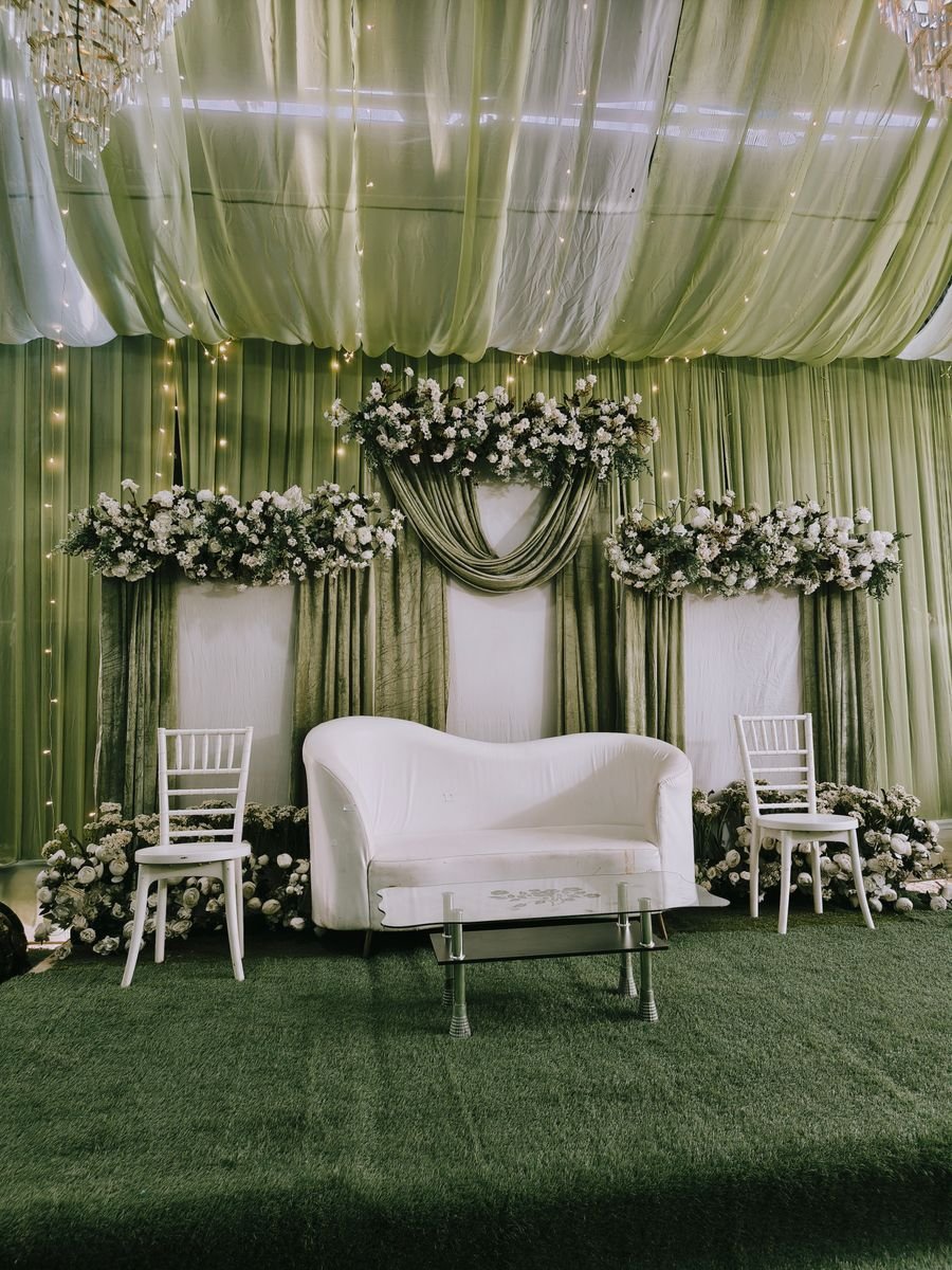 Sage green draped wedding stage with floral arrangements